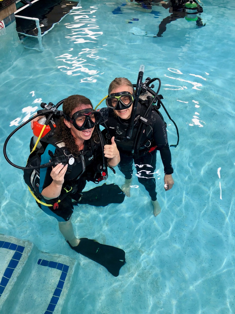 Two women in wet suits stand inside a swimming pool