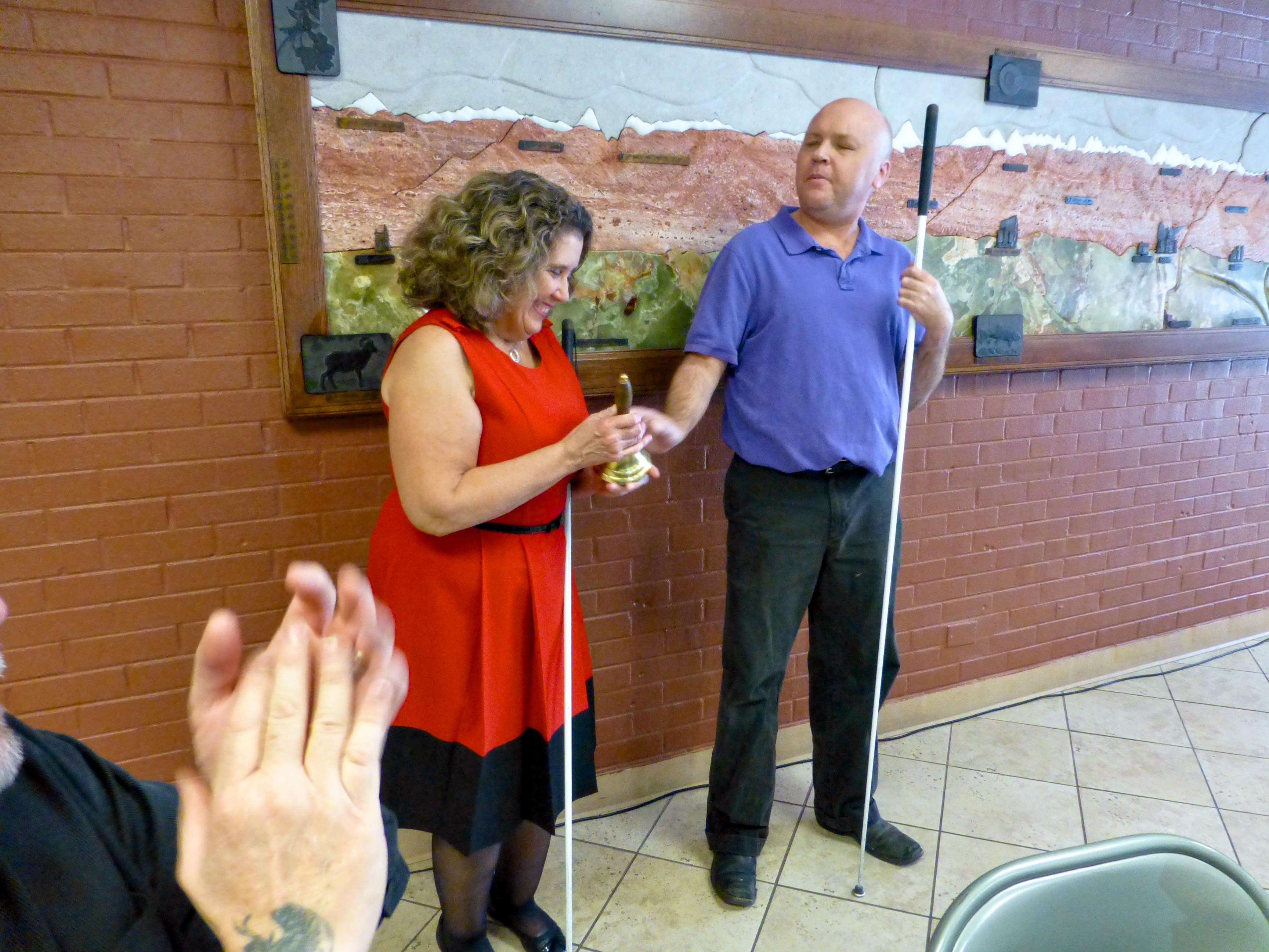 A man hands a woman a hand bell