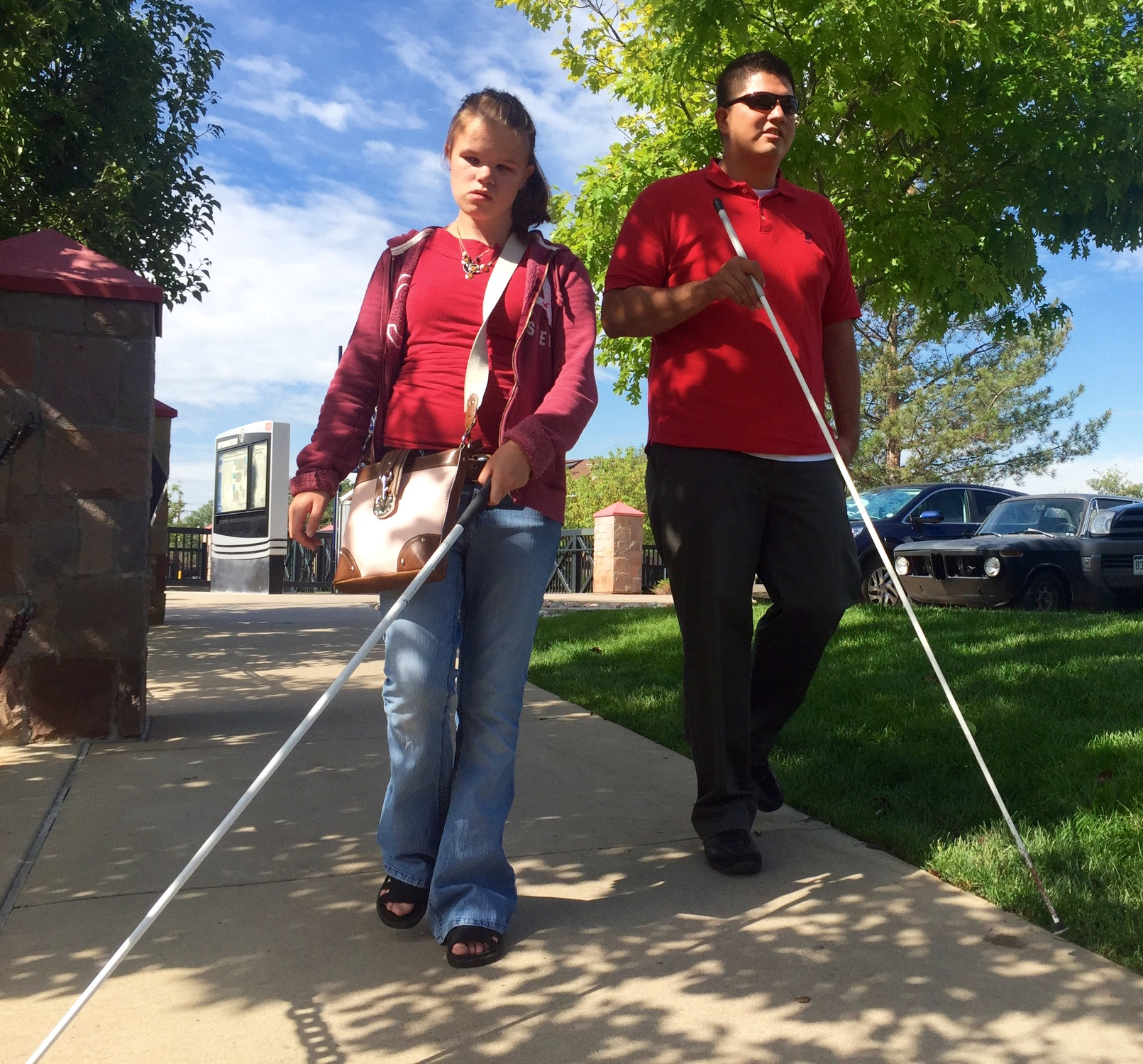 Vika and Martin walk along a shaded sidewalk toward Littleton Downtown Station