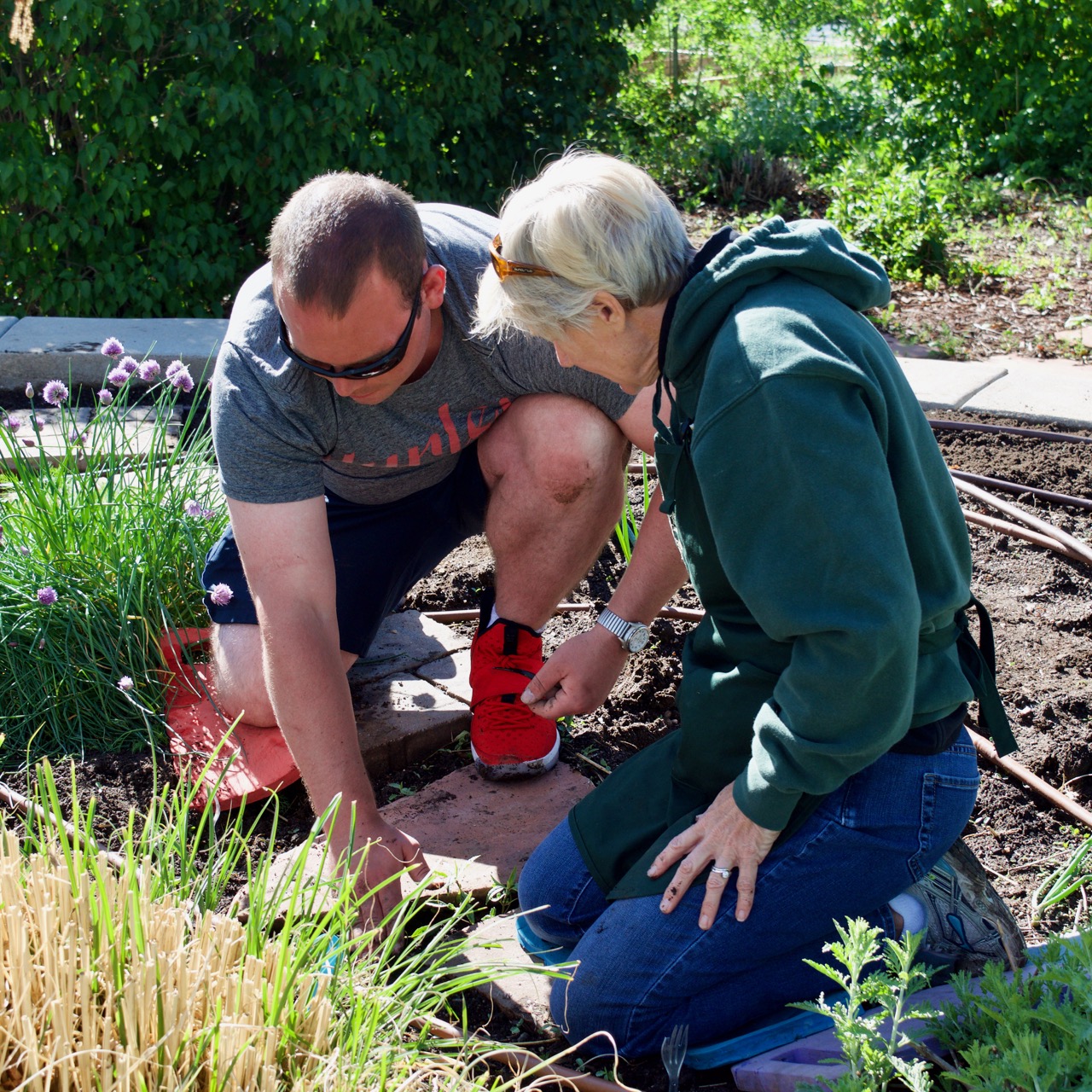 Zach H. on one knee with one of the Master Gardeners planting zucchini in the center of the garden