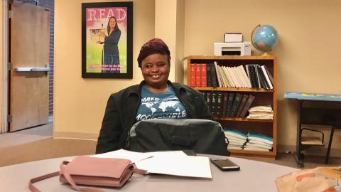 Adama sitting at the table in the travel lobby with her phone and her slate and stylus.