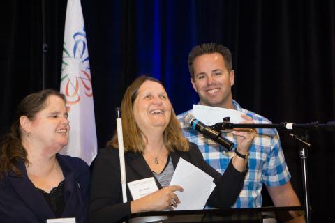 Marc Greytak presents check to Julie Deden at podium, Maryann Migliorelli looks on