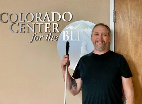Fitz stands and smiles with his White Cane near the CCB Logo