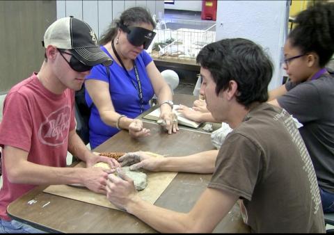 Wearing sleepshades, Jackson and Blanca work with 2 ACC students on arranging items for thermaform sculptures