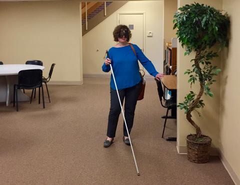 a woman wearing sleep shades uses her cane to maneuver in the Travel Lobby