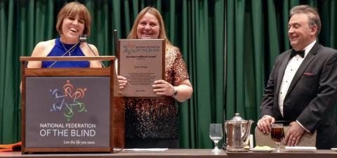 Pam Allen stands at the podium beside Julie Deden holding the Jacobus tenBroek Award in front of her as President Riccobono looks on.