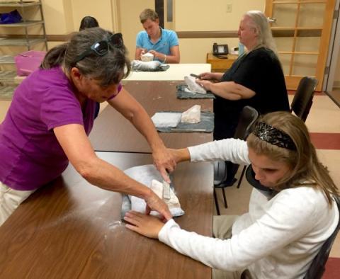 Two women practice the use of a file on a white stone