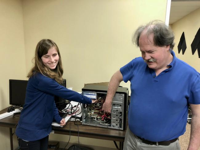 Smiling student explores the inside of a computer with her instructor