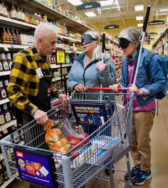 Two In Charge Students push a shopping cart at the grocery store and stop to work with their shopping Assistant near the olives