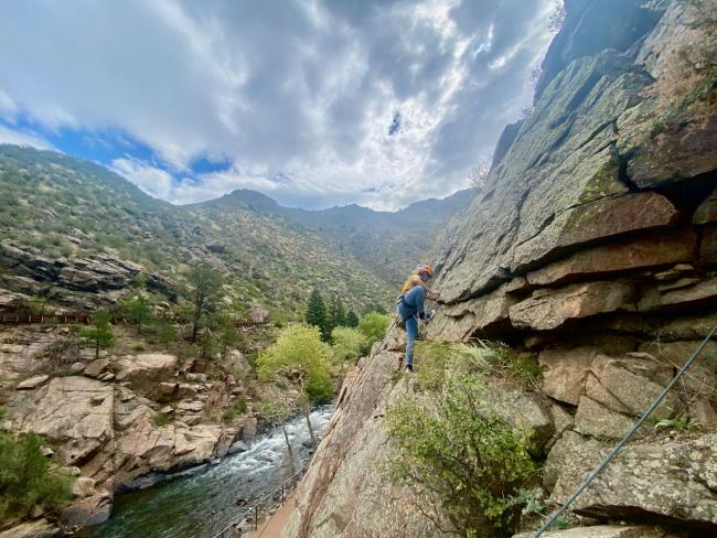 Young man rock climbing with wide canyon and river view