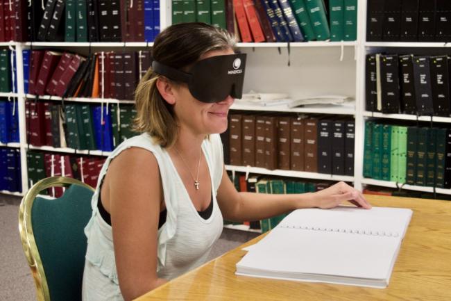 A young woman wearing learning shades reads a braille book.
