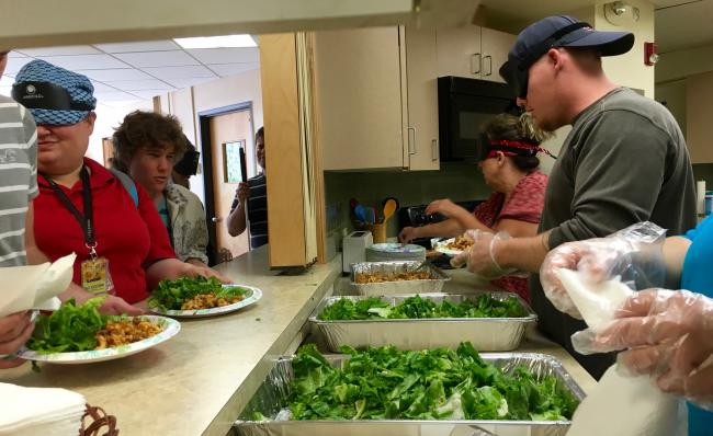 Looking across the serving in the kitchen  multiple trays of food being served to a long line of people visible through the serving window