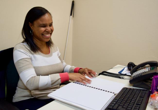 Monique reading Braille at her desk in her office at work