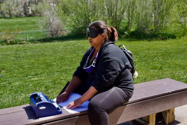Ta'lia reading Braille outside on a bench