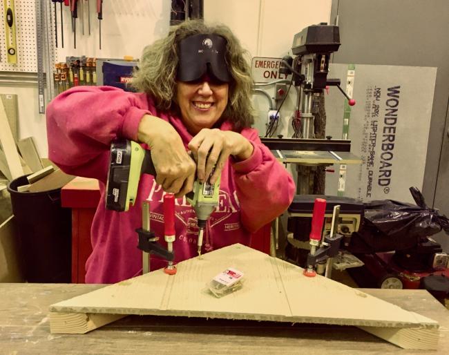 Vicki smiles while using power tools in woodshed.