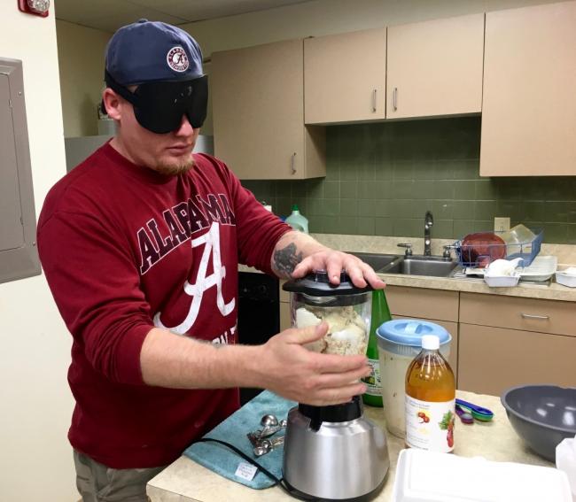 A trim man with dish towel over his shoulder pours a thick white mixture from a bowl to a pan
