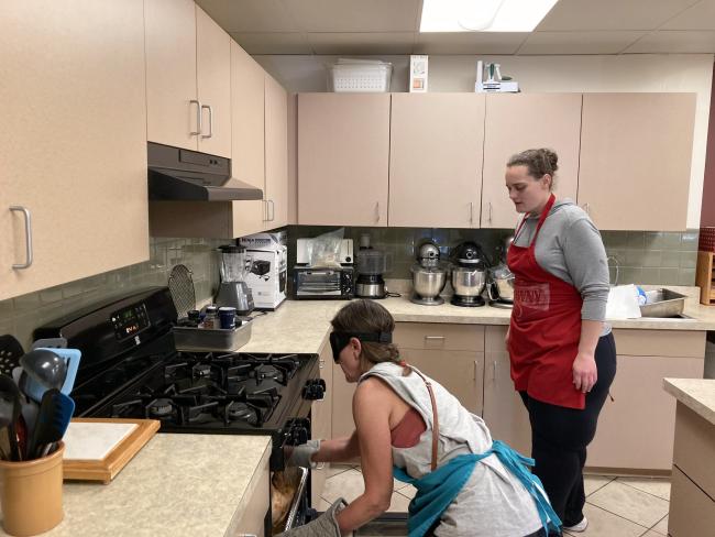 Brittany looks on as Yelena removes  a brown turkey from the oven