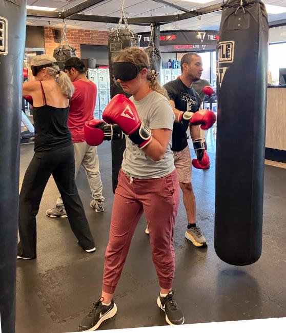 Olivia, Ernesto, Teri, and Jonathan in boxing gloves punch body bags