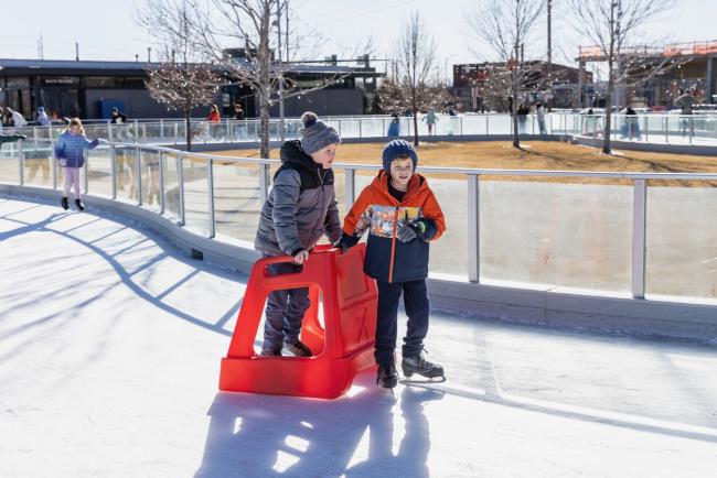 Two youth ice skating with plastic sled 