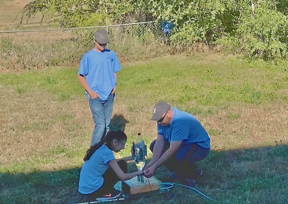A young girl kneels to prepare her rocket for launch.