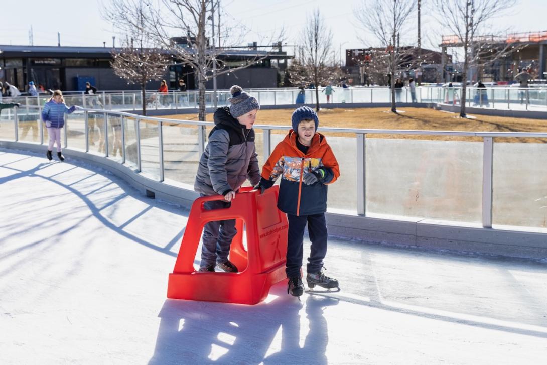 Two youth ice skating with plastic sled 