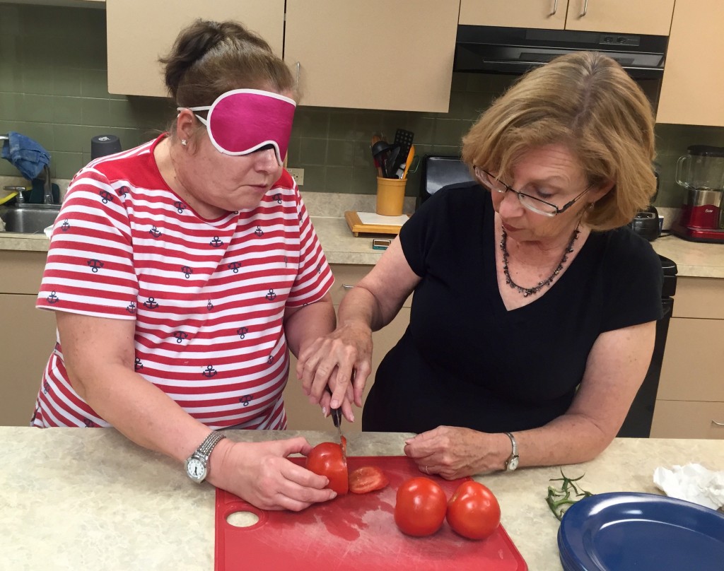 Two women working on knife skills, one wears sleepshades