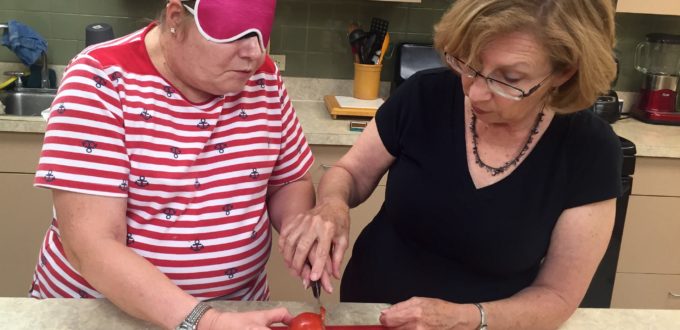 Two women working on knife skills, one wears sleepshades