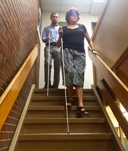 A young man gives a senior woman a cane lesson on the stairs