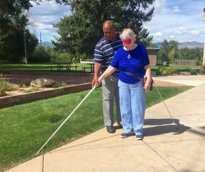 Wayne works with Judy under sleepshades outside the front of the Center showing her how to hold the cane and get good feedback from the edge of the sidewalk and the grassy area