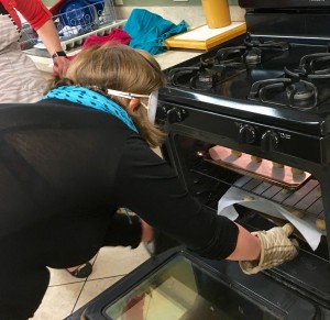 A woman in sleepshades slides a batch of cookies into the oven