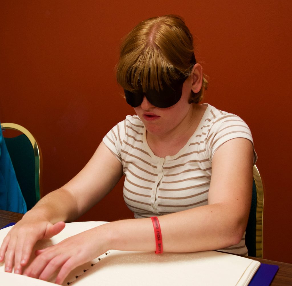 Young woman wearing sleepshades focuses on reading Braille