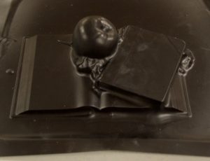 A black plastic sheet impressed with an apple atop one open and one closed book