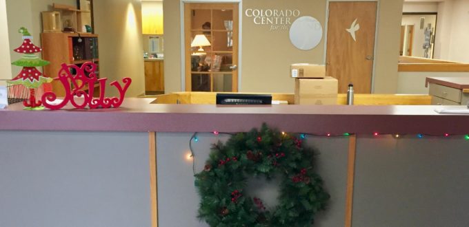 A wreath hanging on the front desk, Christmas lights and wooden ornaments - a Christmas Tree and the word Jolly