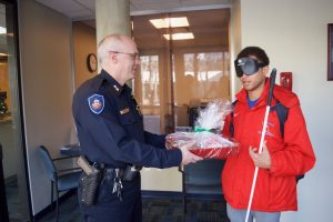 Chaz presents a Christmas basket of items prepared by CCB students to an officer from the Littleton Police Department