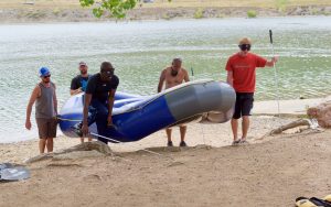 Jimmi, Trevor and Warren help carry a large raft from the lake up to the shore using their canes