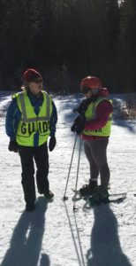 Ellen with ski poles and snowshoes next to her guide on the slope