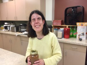 a smiling young woman holds a quart jar of amber appplesauce