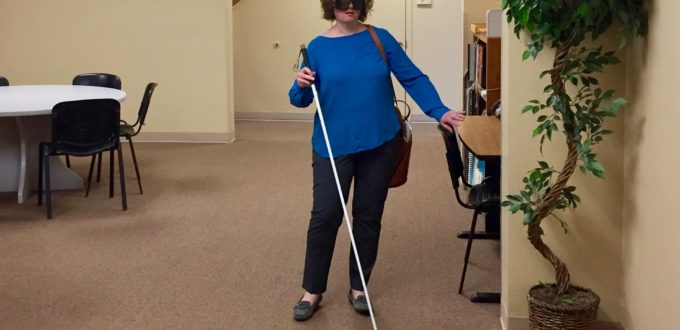 a woman wearing sleep shades uses her cane to maneuver in the Travel Lobby.