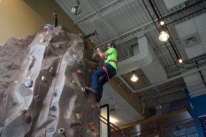 Zach P. reaches the top of the climbing wall and reaches for the bell