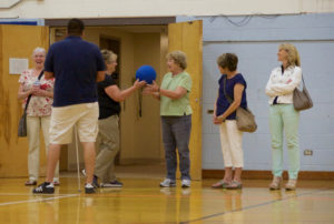 Two women pass a large ball with perforations back and forth in the gym