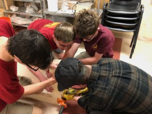 Scott, Stephan, Lucas and Jonathan work together on the floor to attach a leg to the top of one of the new benches