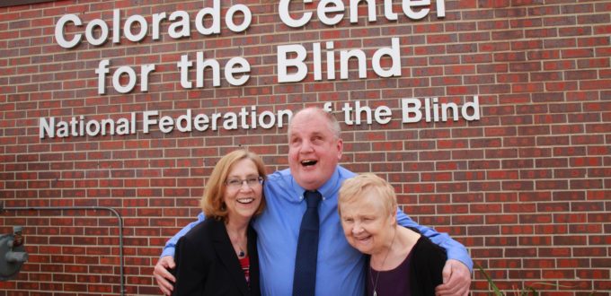 Duncan, Tom and Diane hug in front of the CCB sign on a bright spring day.