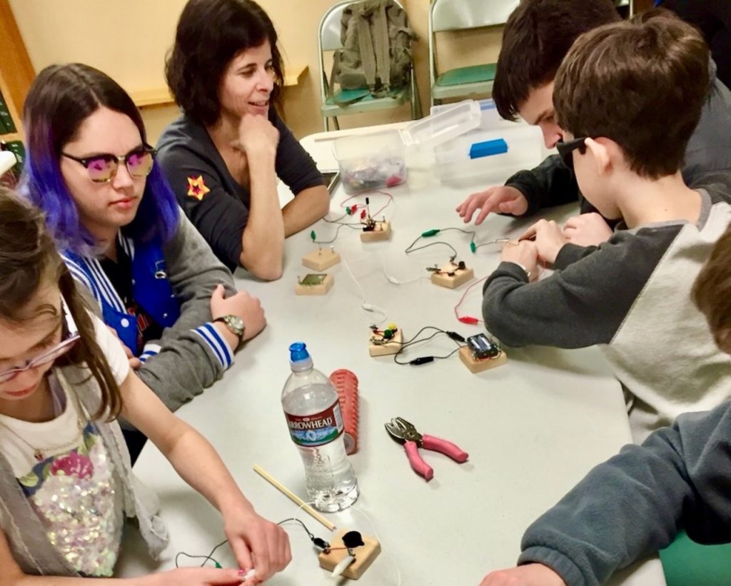 A view down the table of blind youth getting hands on experience making simple circuits