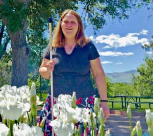 Julie stands behind white iris plants with multiple booms in the Center's front garden.