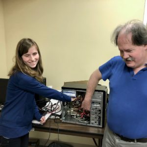 Smiling student explores the inside of a computer with her instructor