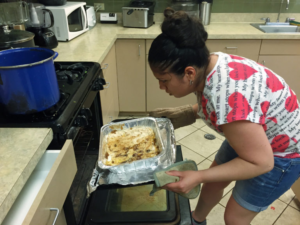A student uses a pot holder and oven mitt to take a large hot pan with Peach Cobbler out of the oven.