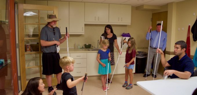 Ernesto talks about travel techniques while 3 children and one adult practice walking with white canes