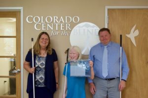 Sixth-grader Chloe stands between Julie and Brent with the tactile CCB logo behind them.