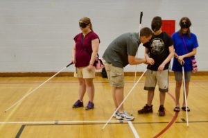 Garret works with Faye, Garrett T.,and Kayla in the Gym on holding their canes properly