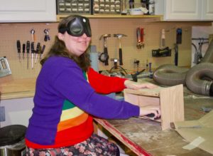 Holly in Woodshop hand sanding a display case she is making for her Bell of Freedom